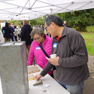 woman and man standing at a table under a canopy in a cemetery, looking at Chinese writing on a gravestone lying on the table