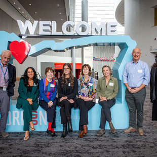 8 people are infront of a light blue cutout of Oregon, 5 are sitting in the cutout, 3 are standing
