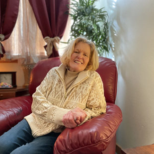 Portrait of a senior woman similing, sitting in a living room in an overstuffed leather chair. 