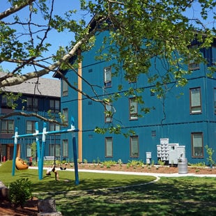 Grassy plaza between multifamily housing buildings with a swingset in the middle.