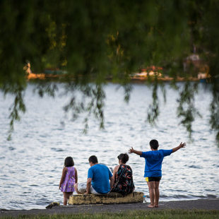 four people -- two adults and two children -- seen from behind facing Blue Lake. The adults are seated, while the children stand, one of them with their arms outstretched.