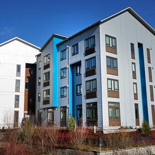 A four-story multifamily building with white, blue and grey exterior finish. 