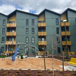 Four story apartment building with green siding and yellow accents. A playground is in the foreground.