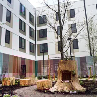 Apartment building courtyard with landscaping and stump seating and young trees.