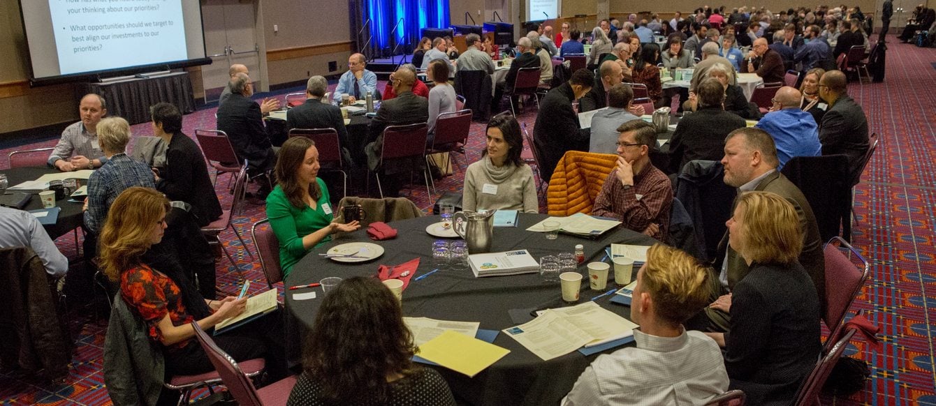 In a ballroom at the Oregon Convention Center, people discuss the future of transportation projects