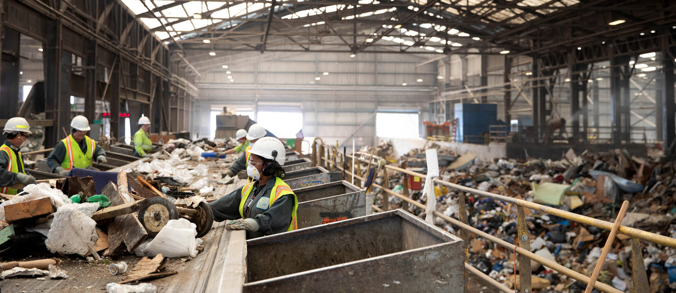 workers near a conveyor belt sort recyclable material from garbage