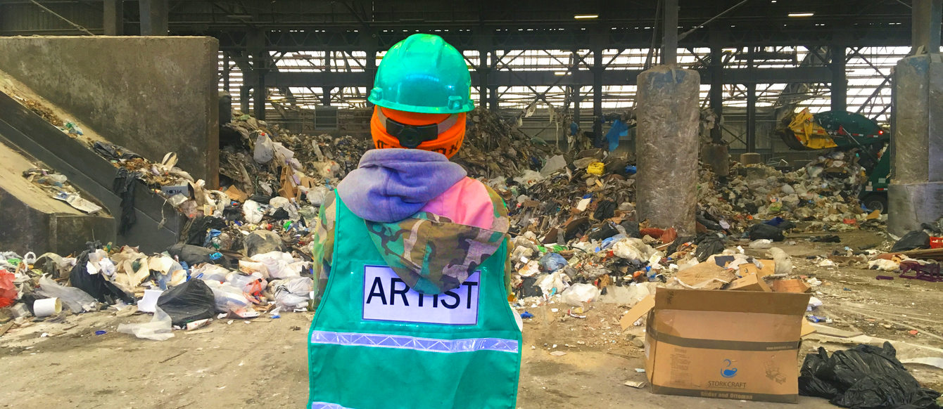 Artist in green safety vest stares at a giant pile of garbage