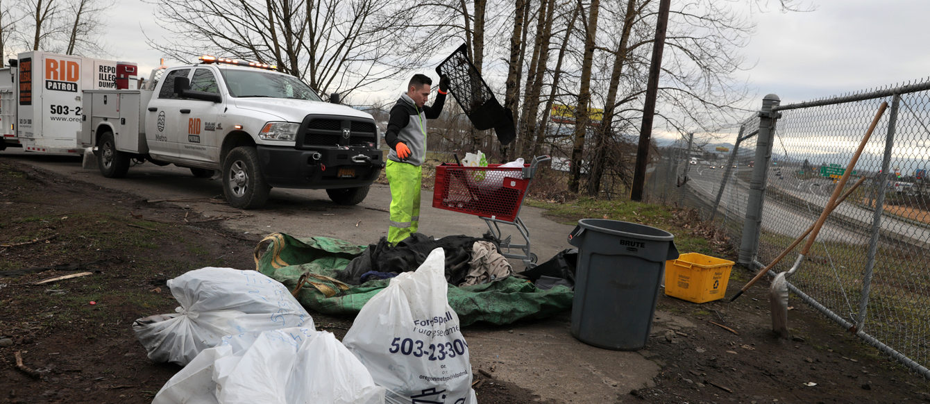 A man goes through dumped garbage on a bluff overlooking a highway