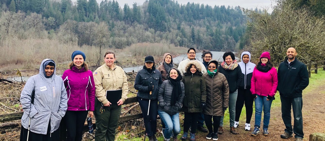 Group of 14 people standing on trail taking group photo with river and forest in background on cloudy winter day