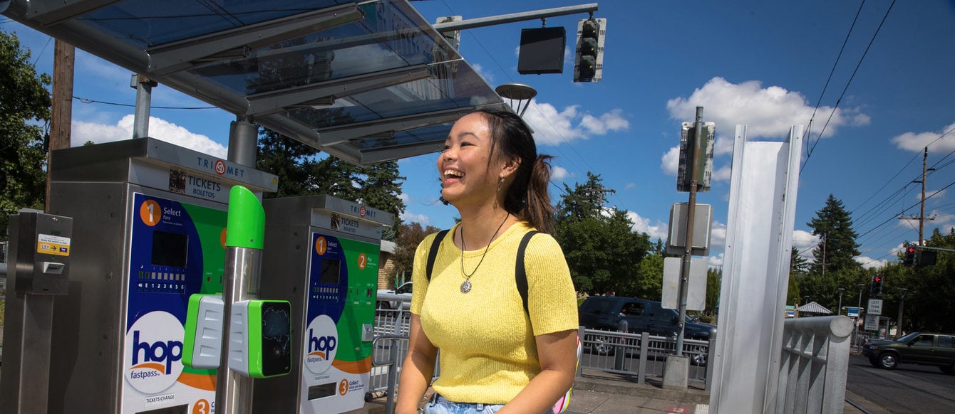 a young woman stands on a MAX train platform holding her fare pass