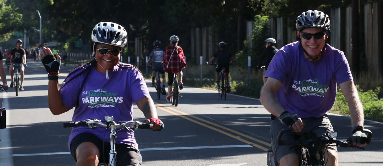 man and woman wearing purple Sunday Parkways t-shirts while riding their bikes