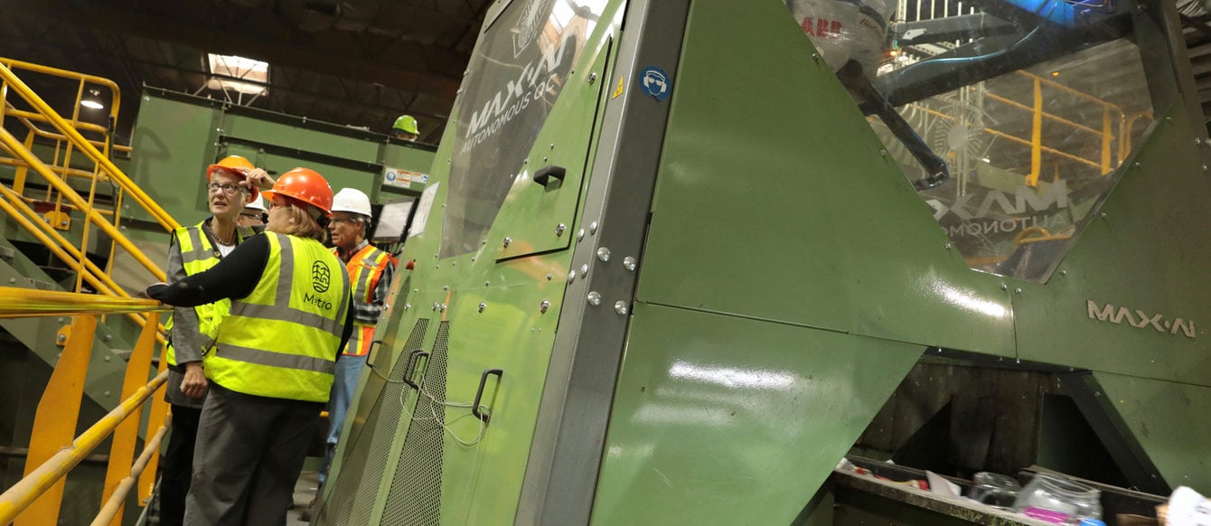 Metro counselors in hard hats check out a recycling conveyor belt that uses robotic arms to sort materials 