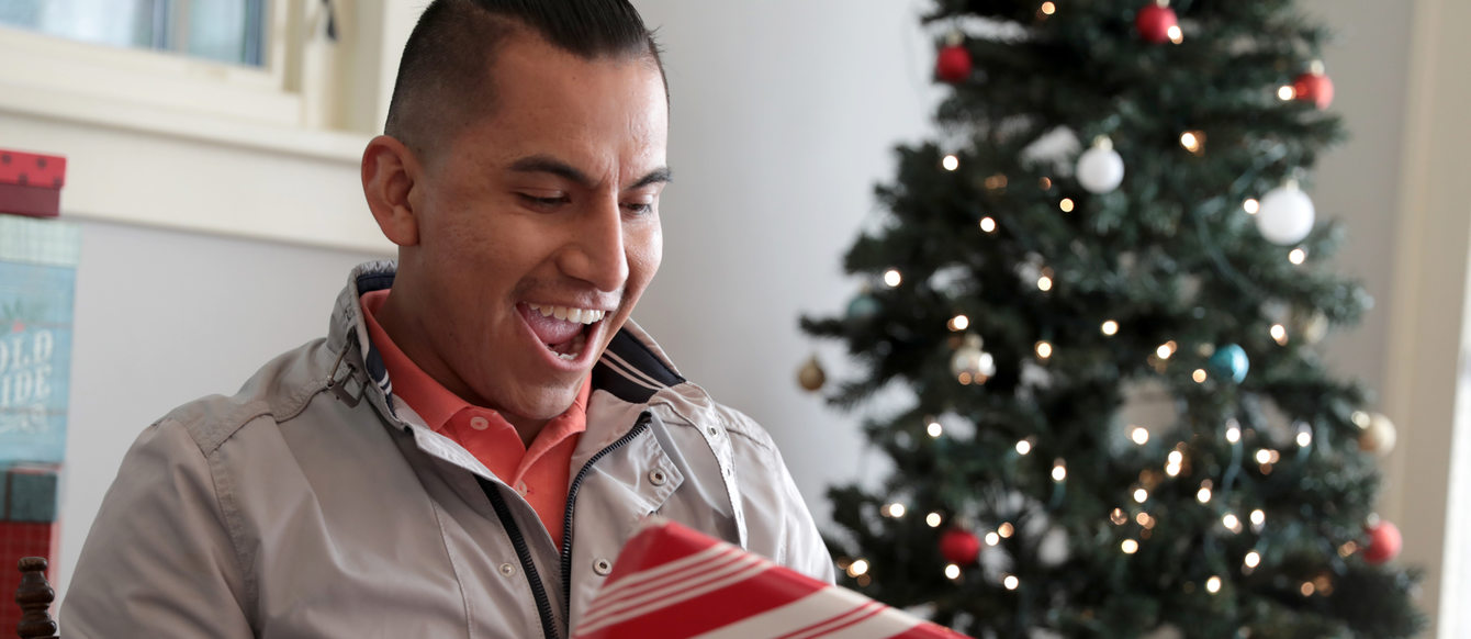 A man reacts with excitement to a festively wrapped holiday present