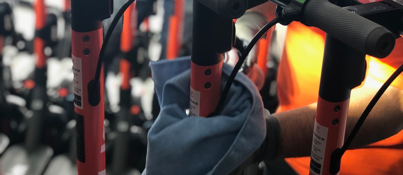 a worker sanitizes a bike in a bikeshare program with a cloth and disinfectant