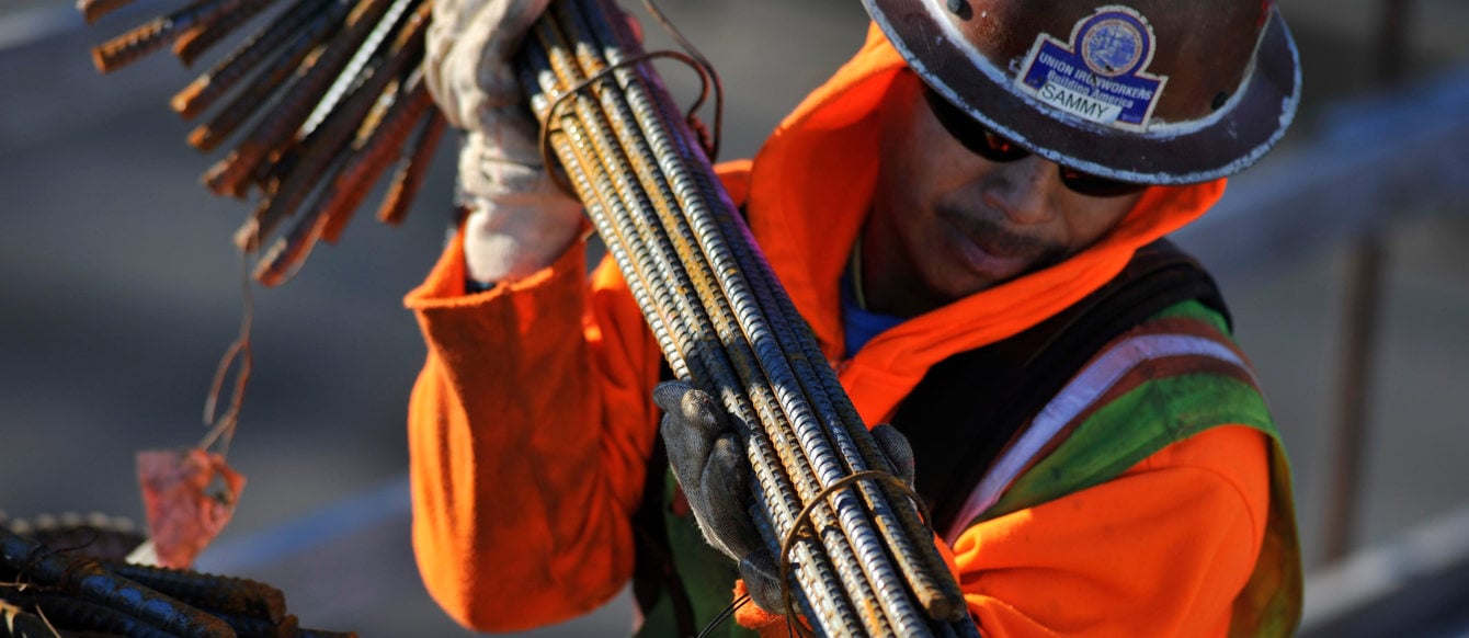 a construction worker carries a bundle of metal rebar at a construction site