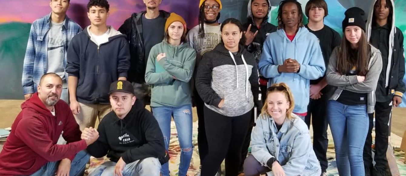 Young artists pose for a picture in front of a mural in progress