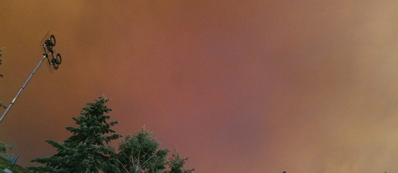 Red and orange smoke billows above a home with large trees in the background.