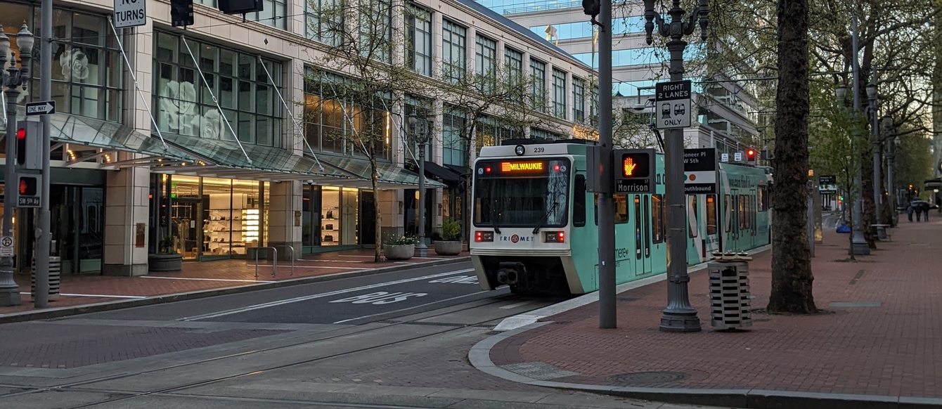 MAX light rail train on an empty street in downtown Portland, with bare-leaved trees and city buildings in the background