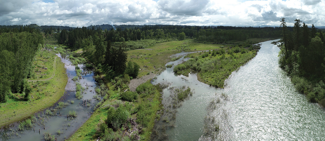 In a drone image, a large river meets a smaller one, with green, tree-filled fields between them.