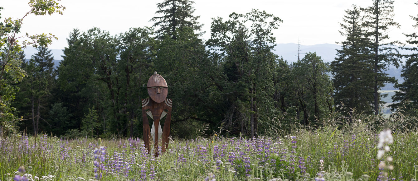 Statue centered in the midst of Doug fir background and lupine in peak bloom.