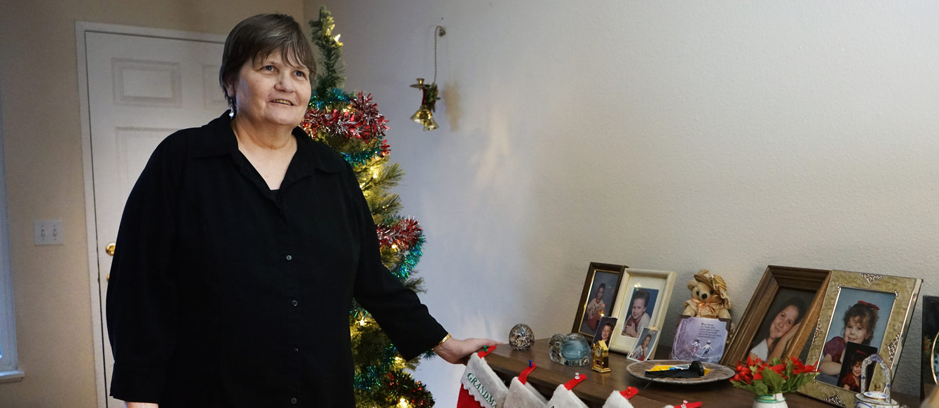 Woman with short hair in black shirt in front of Christmas tree. Her hand is resting on a table with Christmas stockings hanging off the edge.