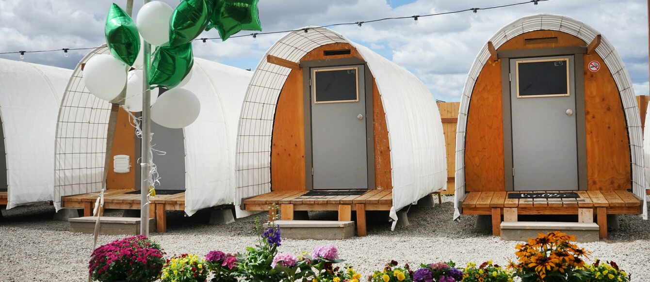 Row of small structures with curved white roofs and wood frames, with row of potted flowers in foreground