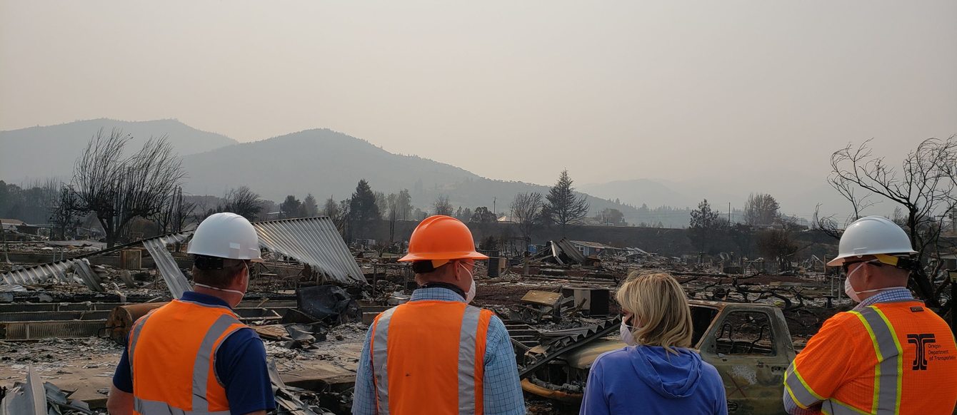 Officials in orange vests survey a debris after a wildfire