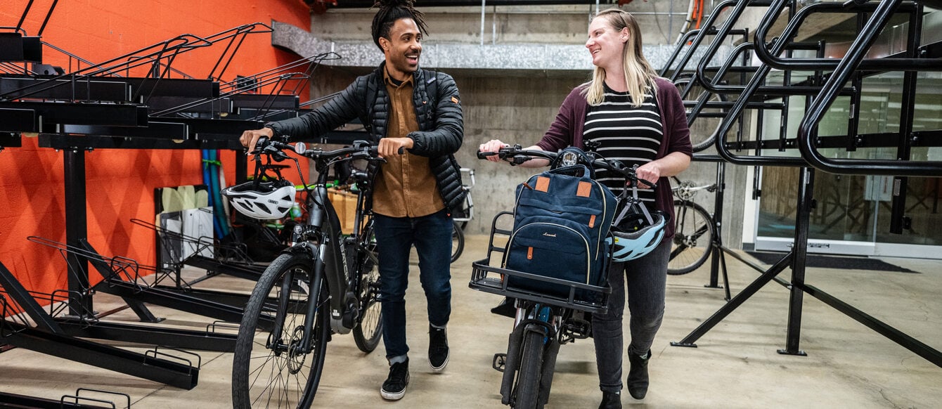 Two people walk with their bikes in a bicycle storage room.