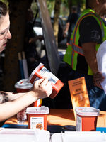 One woman shows a quart-sized sharps container to another woman while at an event. A man in a safety vest stands in the background. 