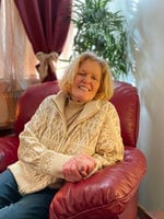Portrait of a senior woman similing, sitting in a living room in an overstuffed leather chair. 