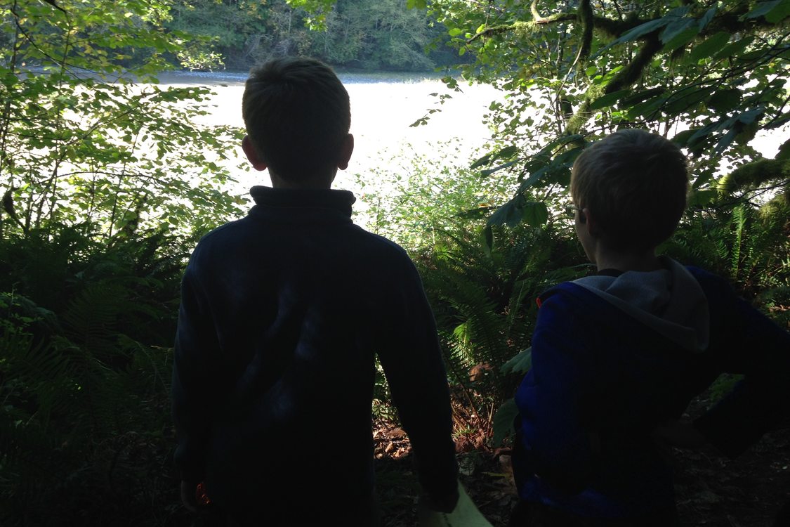 two children looking through trees at a river in the distance