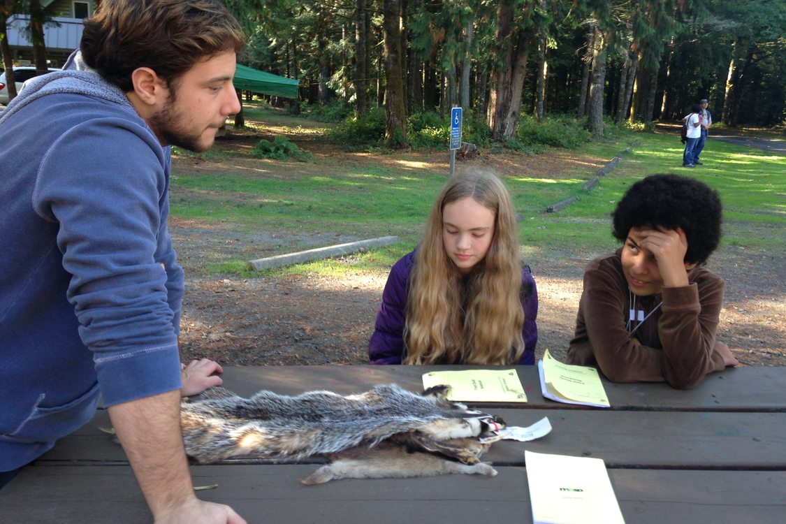 A teacher at Outdoor School shows an animal pelt to two students