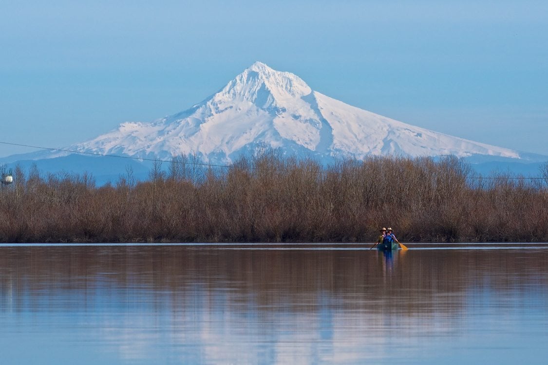 Two people canoeing in a lake at Smith and Bybee Wetlands with Mount Hood in the background