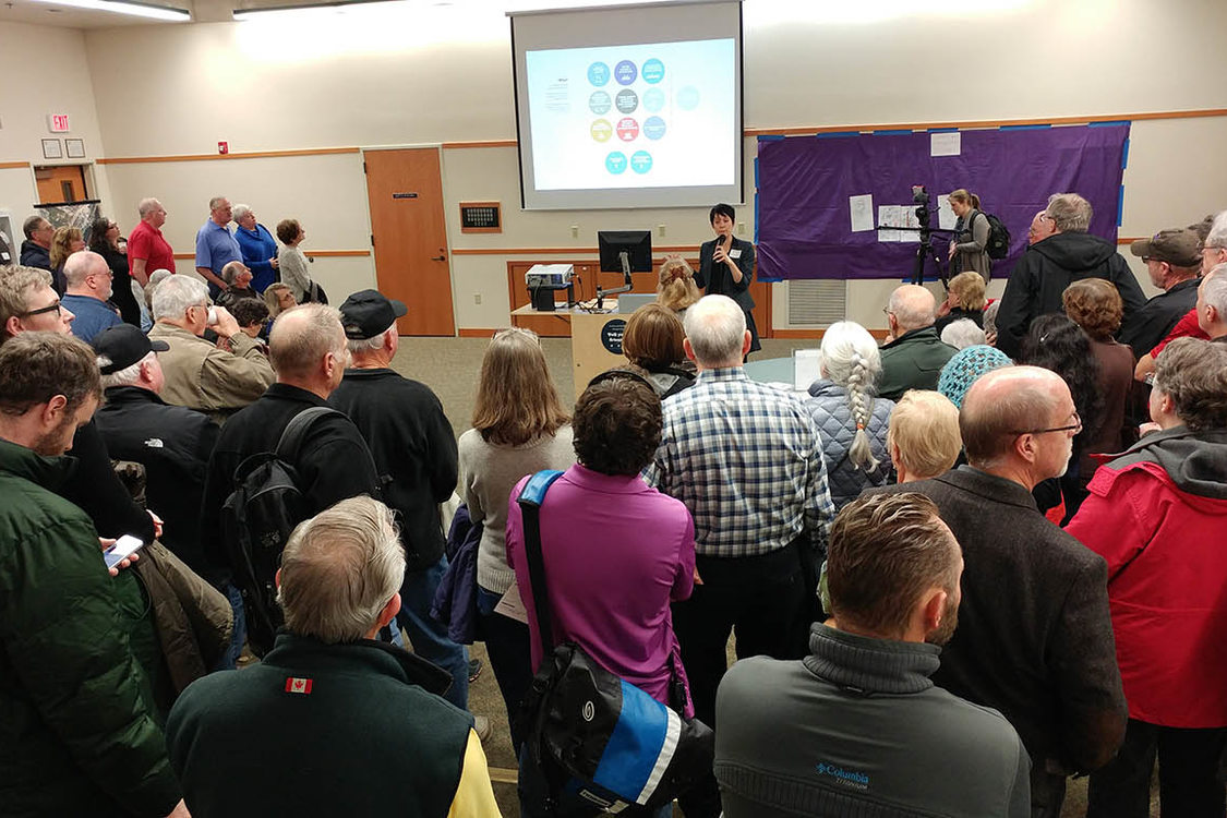 woman presenting a slideshow and speaking to a room full of people