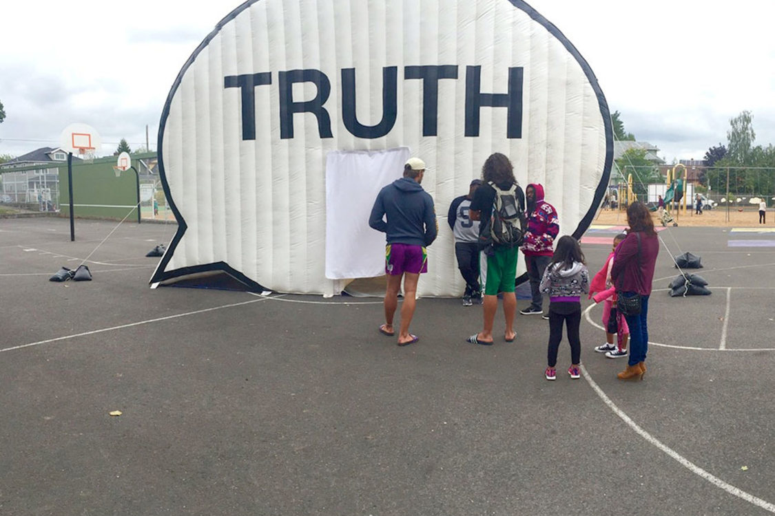 A school's playground with an art exhibit, specifically a tent in the shape of a comment bubble with the word "truth" across it