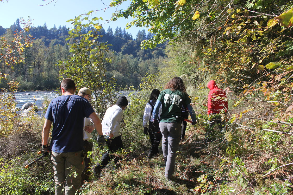 Group of people walking on trail along river banks.