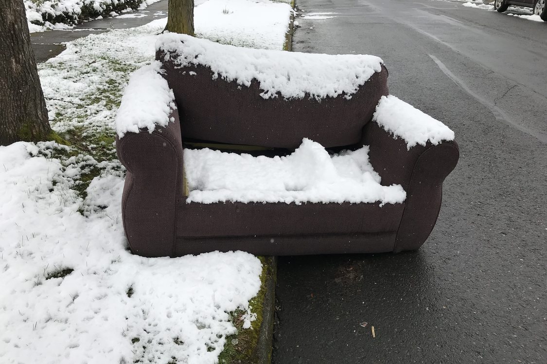 couch on curb with an inch of snow on it