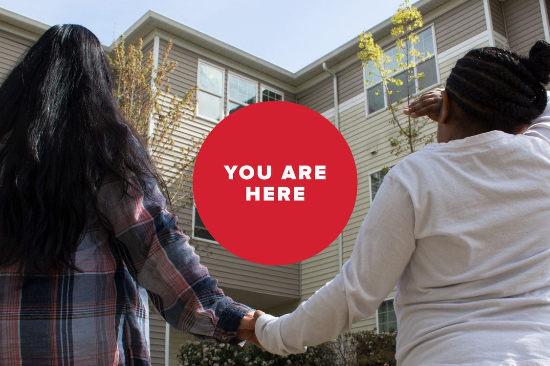 A woman and her daughter hold hands in front of an apartment building