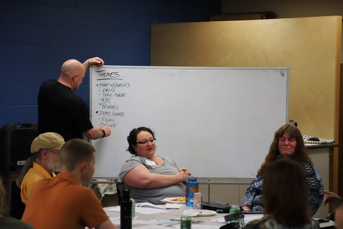 A man takes notes on a white board while community members discuss