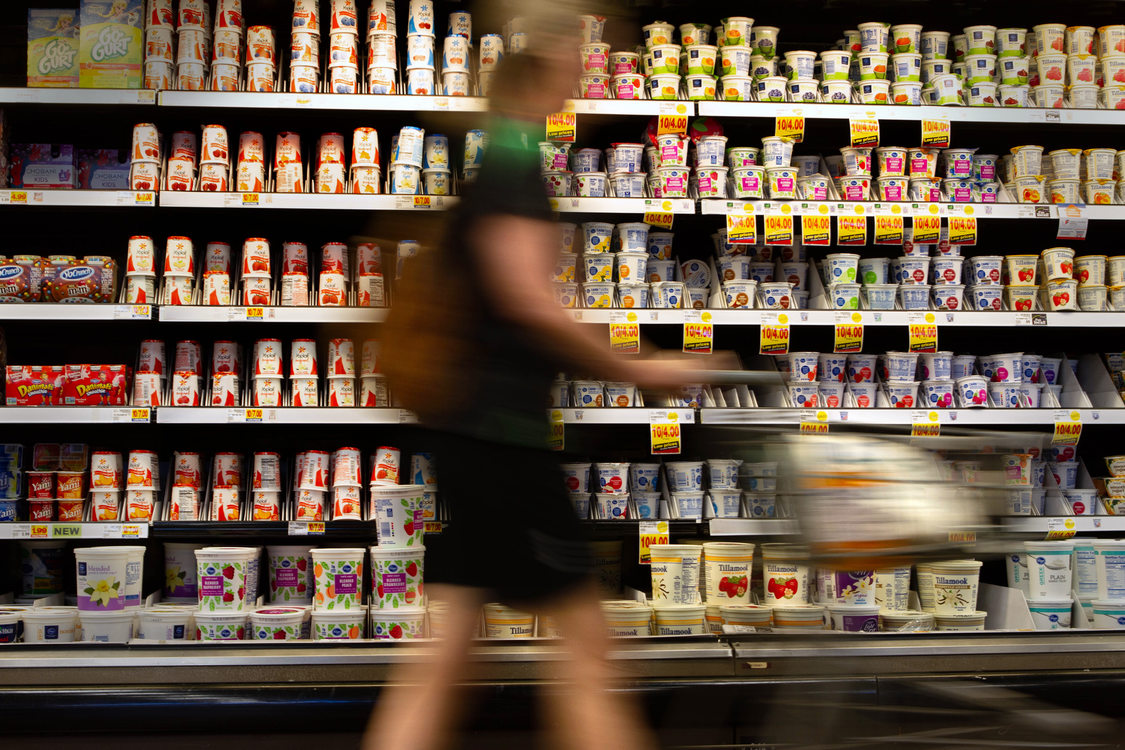 A woman pushes a cart past shelves of yogurt containers