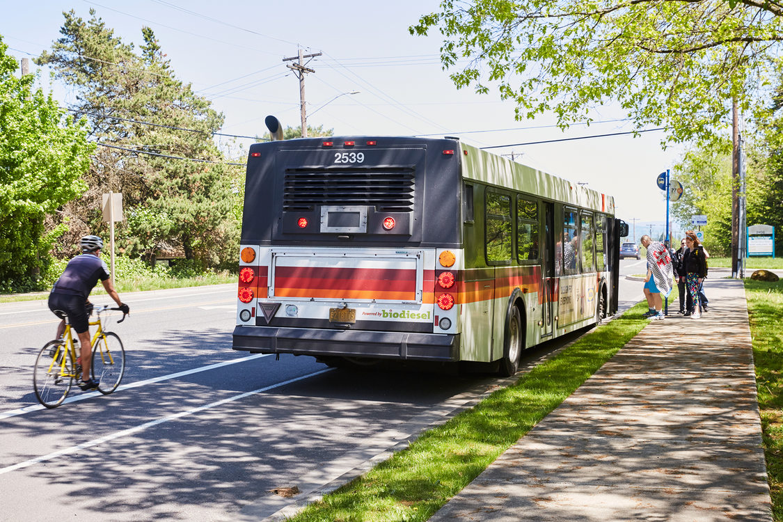 A bus stops for passengers while a bicyclist rides by