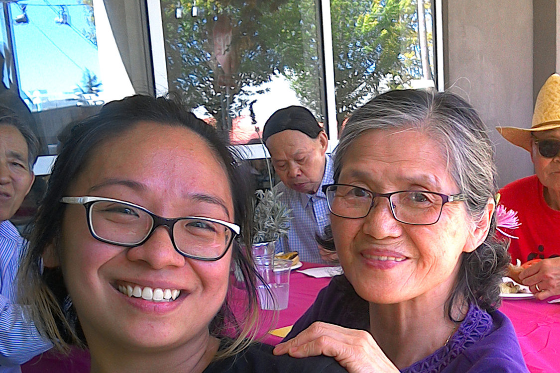 A smiling elder woman sits next to a smiling younger woman at a community event