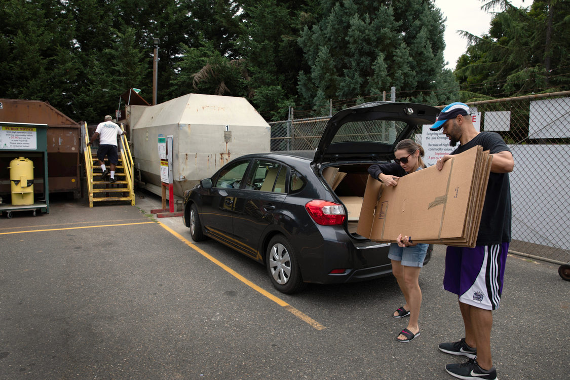 a couple takes a stack of flattened cardboard out of their car