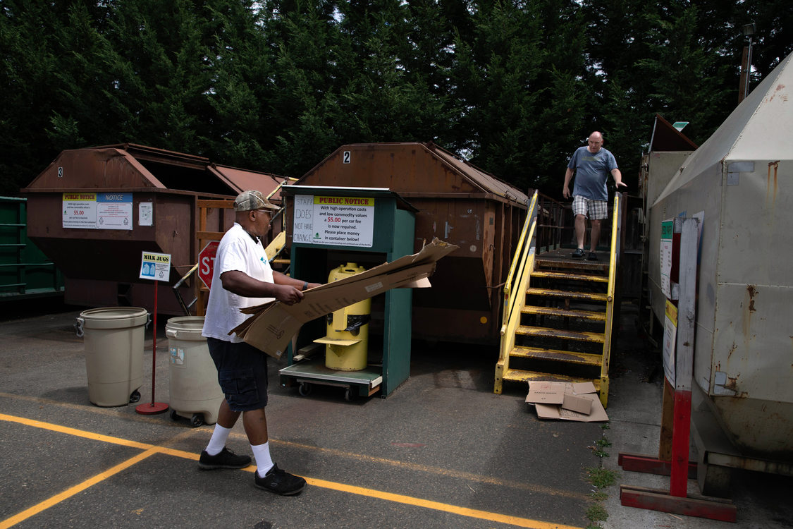 a man carries cardboard to a large metal container