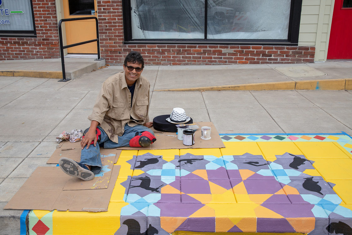 Artist Kanaan Kanaan smiles next to his mural in Tigard