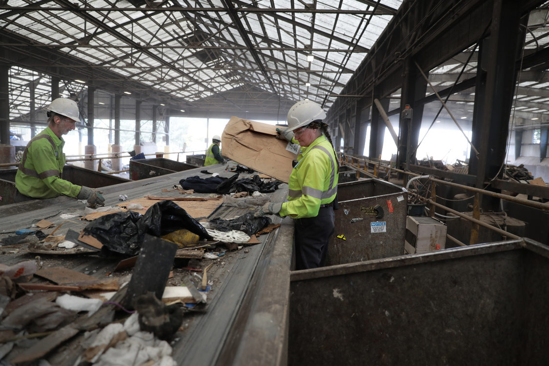 a woman in a hard hat sorts through garbage on a conveyor belt