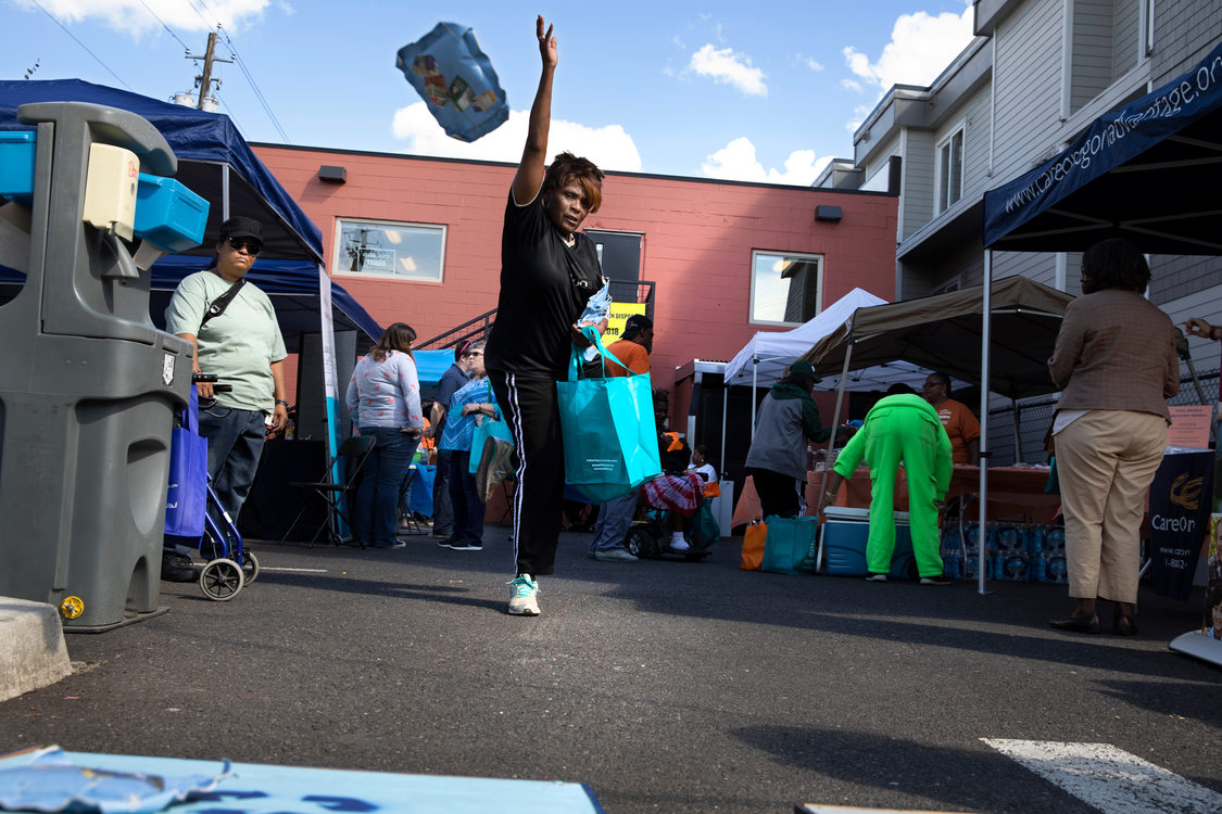 a woman tosses a bean bag in a game of garbage and recycling corn hole