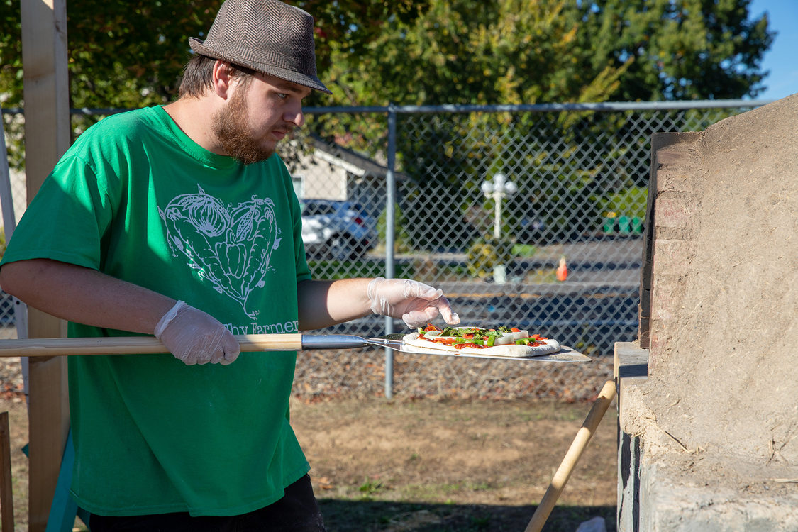 a young man is about to put a pizza inside a cob oven 