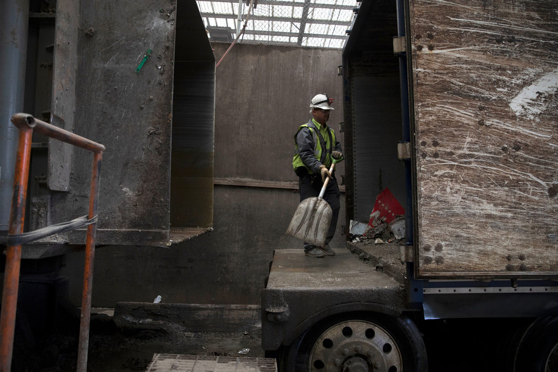 a man in a hard hat shovels loose garbage into the back of a truck trailer