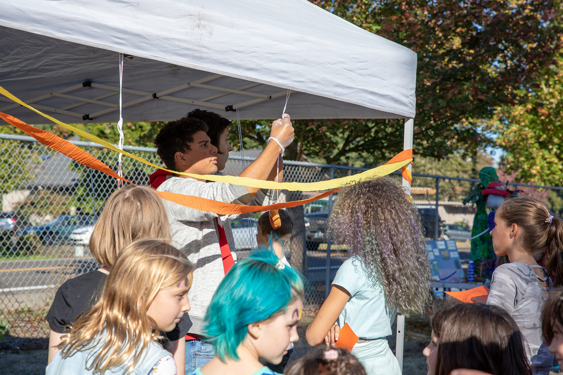 A young man hangs a doughnut from a string while kids crowd around him.